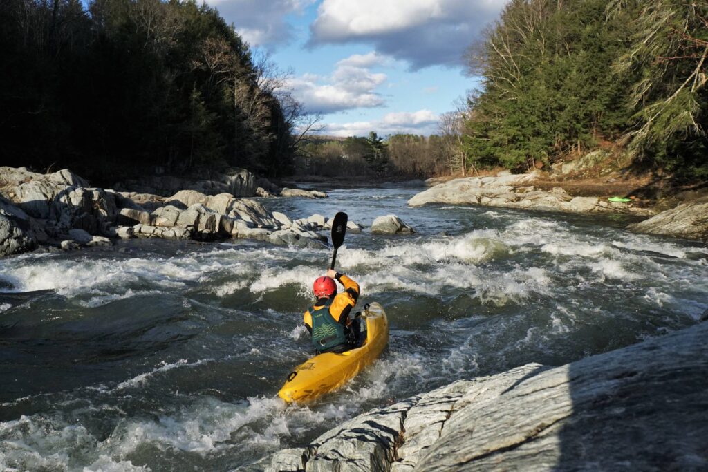 Clay Murphy running the final rapid on the Lower Mad River in evening sunlight. Vermont whitewater kayaking.