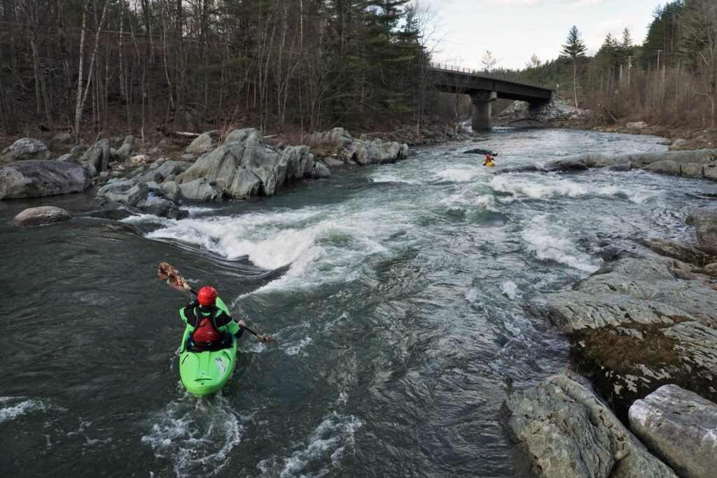 Adam Carparelli heads into S-Turn as Clay Murphy looks on from below. Route 100B bridge visible in the background. Vermont Whitewater Kayaking.